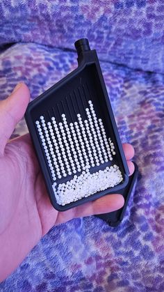 a person holding a black and white device with beads in it's case on a purple blanket