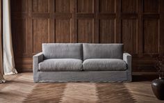 a gray couch sitting in front of a wooden paneled wall next to a vase