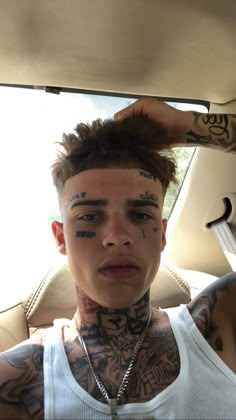 a man with tattoos on his face sitting in a car