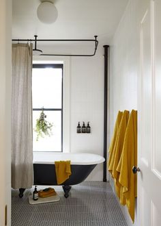 a black and white bathtub sitting next to a window in a bathroom with yellow towels on the floor