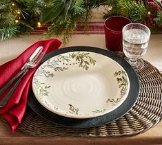 a place setting with red napkins, silverware and christmas greenery on the table