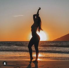 a woman standing on the beach at sunset doing yoga exercises with her arms in the air