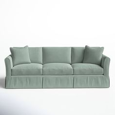 a light green couch with four pillows on the back and one arm folded over it, sitting in front of a white wall