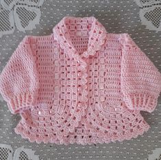 a pink knitted sweater sitting on top of a white lace tablecloth with an openwork design