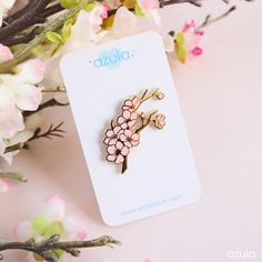 a pink flower brooch sitting on top of a white card next to some flowers