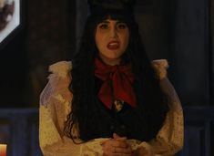 a woman with long black hair wearing a red bow around her neck, standing in front of a lit candle