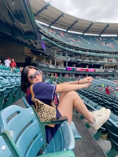 a woman sitting in the bleachers at a baseball game with her hand on her hip