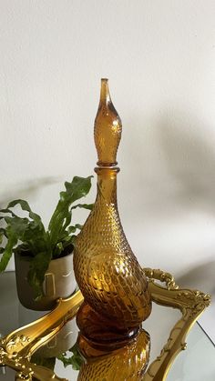 a golden vase sitting on top of a glass table next to a potted plant