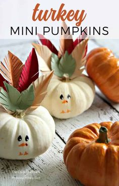 three small pumpkins decorated with paper leaves and turkey faces on them, sitting on a white wooden surface