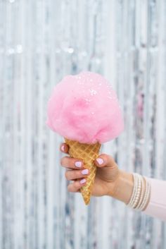 a person holding an ice cream cone with pink frosting on it in front of a wall