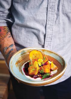 a man holding a plate with food on it in his hand and tattoos on his arm