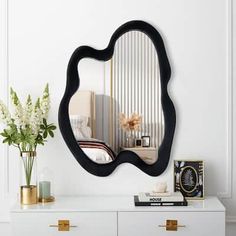 a mirror that is sitting on top of a dresser next to a vase with flowers