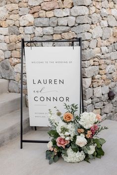 a sign with flowers on it next to a stone wall