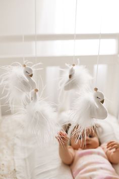 a baby is laying in a crib with white feathers hanging from it's sides