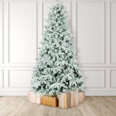 a white christmas tree with presents in front of it on a wooden floor next to a wall