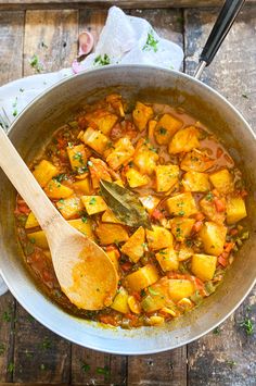 a wooden spoon in a pot filled with food on top of a wood table next to a