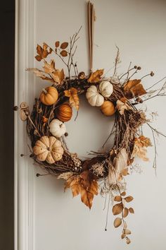 a wreath with pumpkins and leaves hanging on the door handle, in front of a white wall