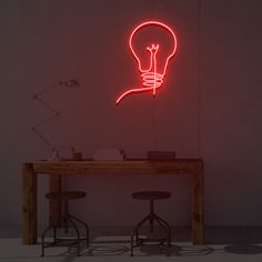 a table with two stools and a neon light bulb on the wall above it