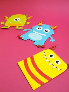 three paper monsters sitting on top of a pink surface