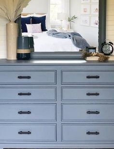 a blue dresser with a mirror above it and a bed in the back ground behind it