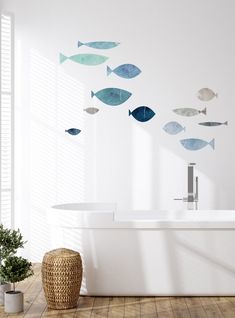 a bath tub sitting under a window next to a potted plant and fish wall decals