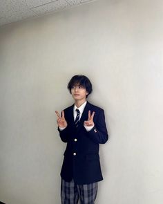 a young man in a suit and tie making the vulcan sign with his hands while standing against a wall