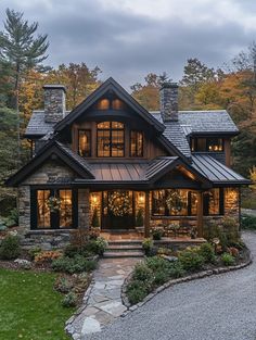 a large house with lots of windows and lights on it's front porch, surrounded by trees