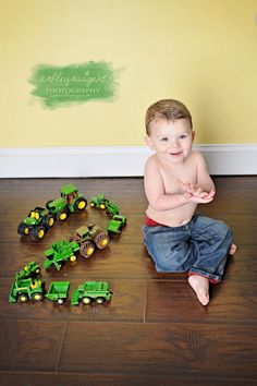 a young boy sitting on the floor playing with toy trucks and tractor toys in front of him