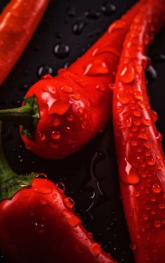 three red peppers sitting on top of a black surface covered in water droplets and raindrops