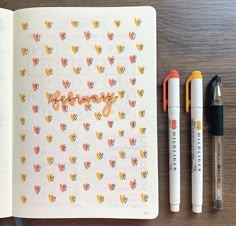 an open notebook with writing on it next to two markers and a pen, which are sitting on top of a wooden table