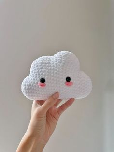 a hand holding up a small white cloud with pink cheeks and eyes on it's face