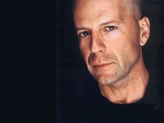 a man with bald head and black shirt looking at the camera while standing in front of a dark background