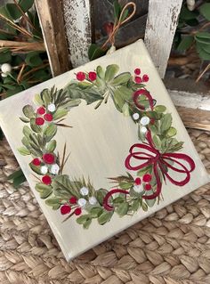 a christmas wreath with holly and berries painted on it is sitting on a wicker chair