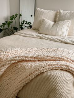 a bed with white blankets and pillows on it's headboard, next to a potted plant