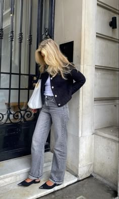 a woman standing on the steps of a building with her hands in her pockets and looking down