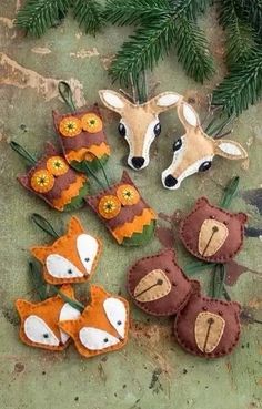 several felt animals are sitting on the ground next to some pine branches and needles with orange flowers