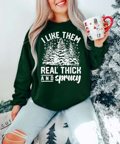 a woman wearing a green sweatshirt holding a coffee mug in front of a christmas tree