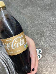 a person holding a bottle of coca - cola in their hand while sitting on the floor