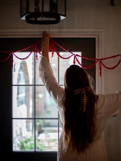 a woman is holding up red string on the window sill with her arms in the air