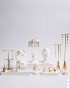 an assortment of white and gold jewelry displayed on pedestals in front of a gray background