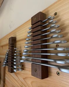 there are many spoons hanging on the wall with wood and metal hooks attached to it