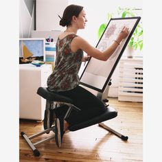 a woman sitting at a desk drawing on a large easel with a black chair