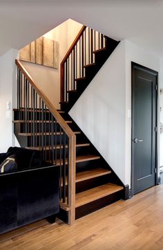 a living room with a black couch and wooden stairs leading up to the second floor