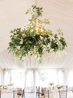 a chandelier filled with flowers and greenery hangs from the ceiling in a tent