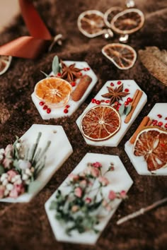 some orange slices and cinnamons are arranged on small trays with flowers, leaves and spices