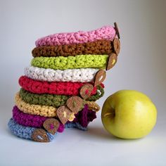 a stack of crocheted cloths next to an apple