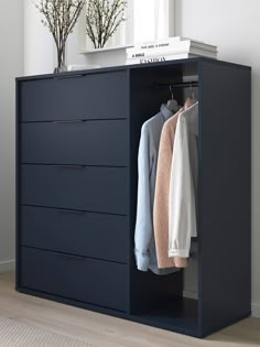 a blue dresser with two shirts hanging on it's sides and a vase filled with flowers