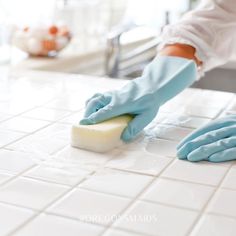 a person in blue gloves cleaning a white tile counter top with a sponge on it