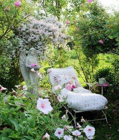 a chair in the middle of a garden with flowers around it and an angel statue next to it