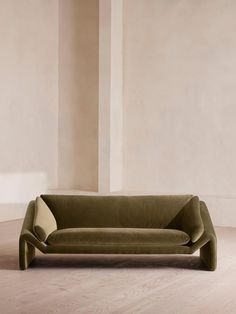 a green couch sitting on top of a hard wood floor next to a white wall